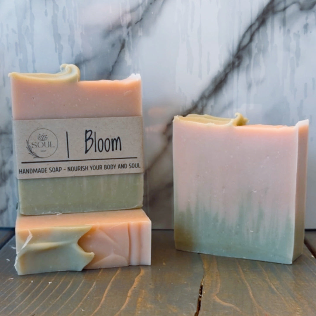 Three handmade soap bars with a 'Bloom' label on a marble surface