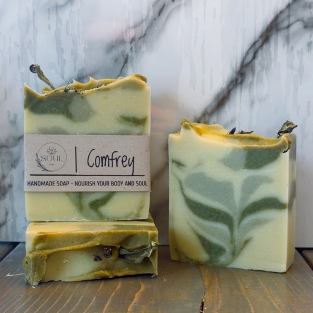 Three handmade soap bars with a visible label with name Comfrey on a marble surface