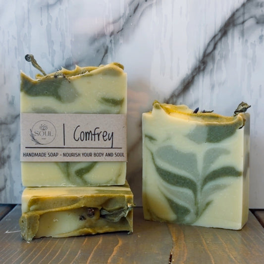 Three handmade soap bars with a visible label with name Comfrey on a marble surface